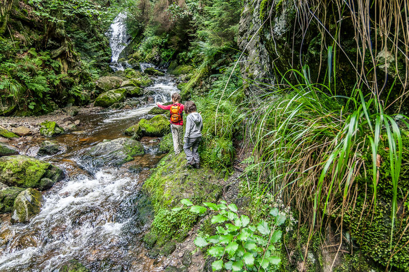 Mädchen balancieren auf moosbewachsenen Steinen neben einem Wasserfall in der Ravennaschlucht im Hochschwarzwald