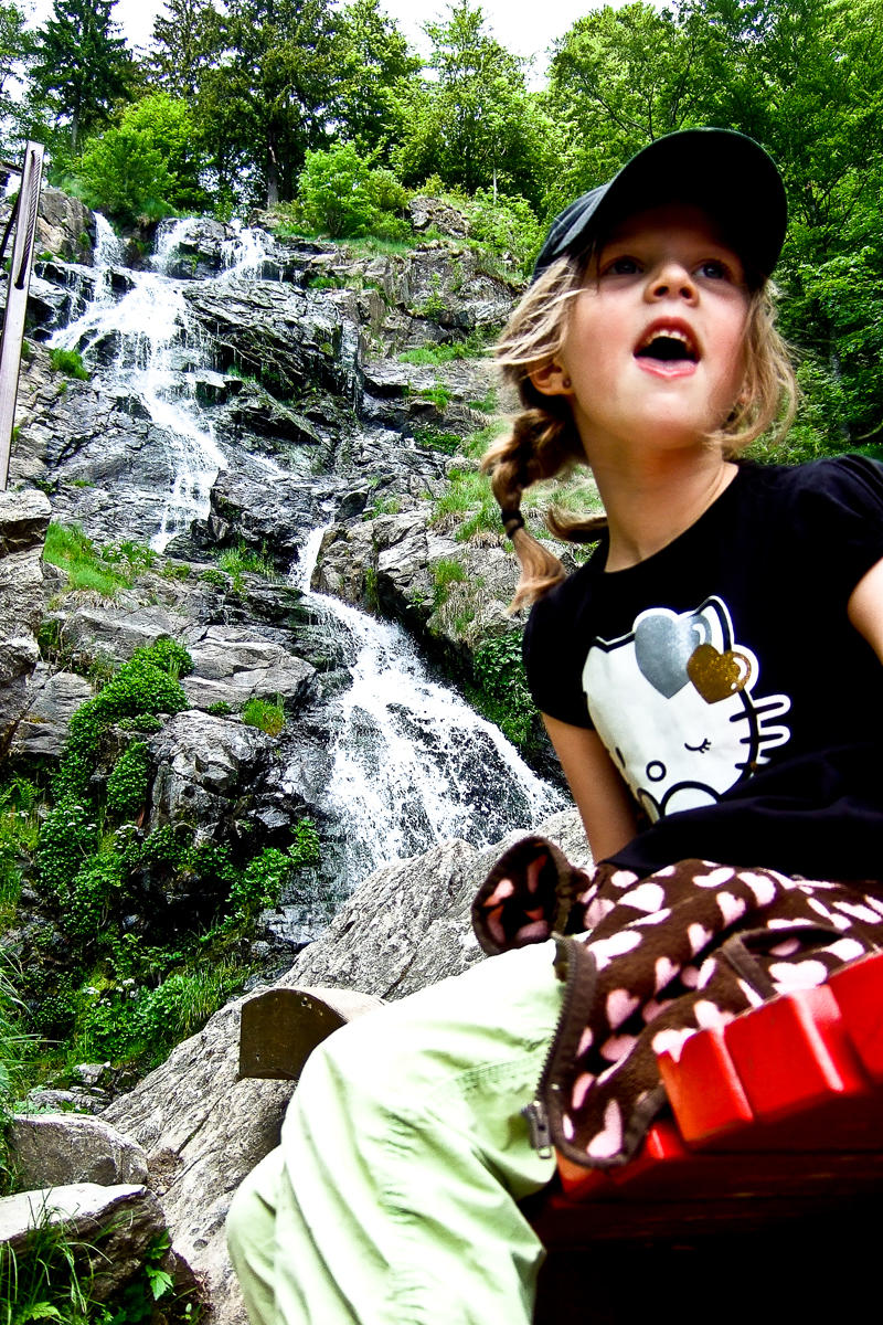 Mädchen mit Hello Kitty T-Shirt sitzt vor der Kulisse des Todtnauer Wasserfalls